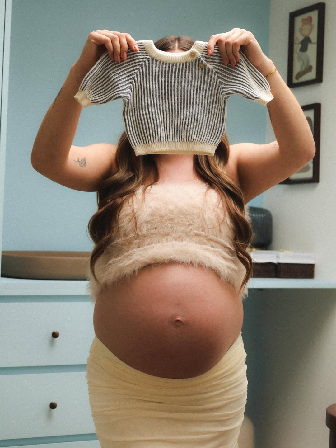 Zwangere vrouw houdt een babytruitje boven haar buik